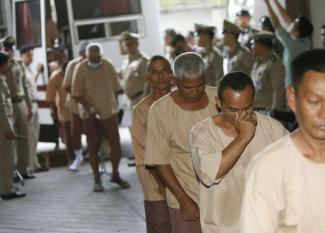 Suspects, allegedly involved in human trafficking of Rohingya migrants, are escorted by prison officials as they arrive at a criminal court in Bangkok on 10 November 2015. More than 150 warrants have been issued against officials suspected of their involvement in the trafficking ring.