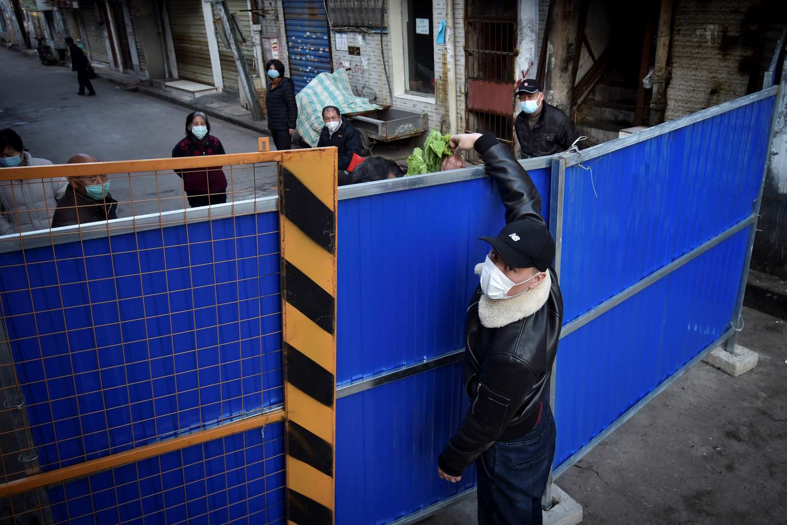 A man passes food through barricades blocking a residential area in Wuhan, China, in early 2020. No country was prepared for the extent of the Covid-19 pandemic.