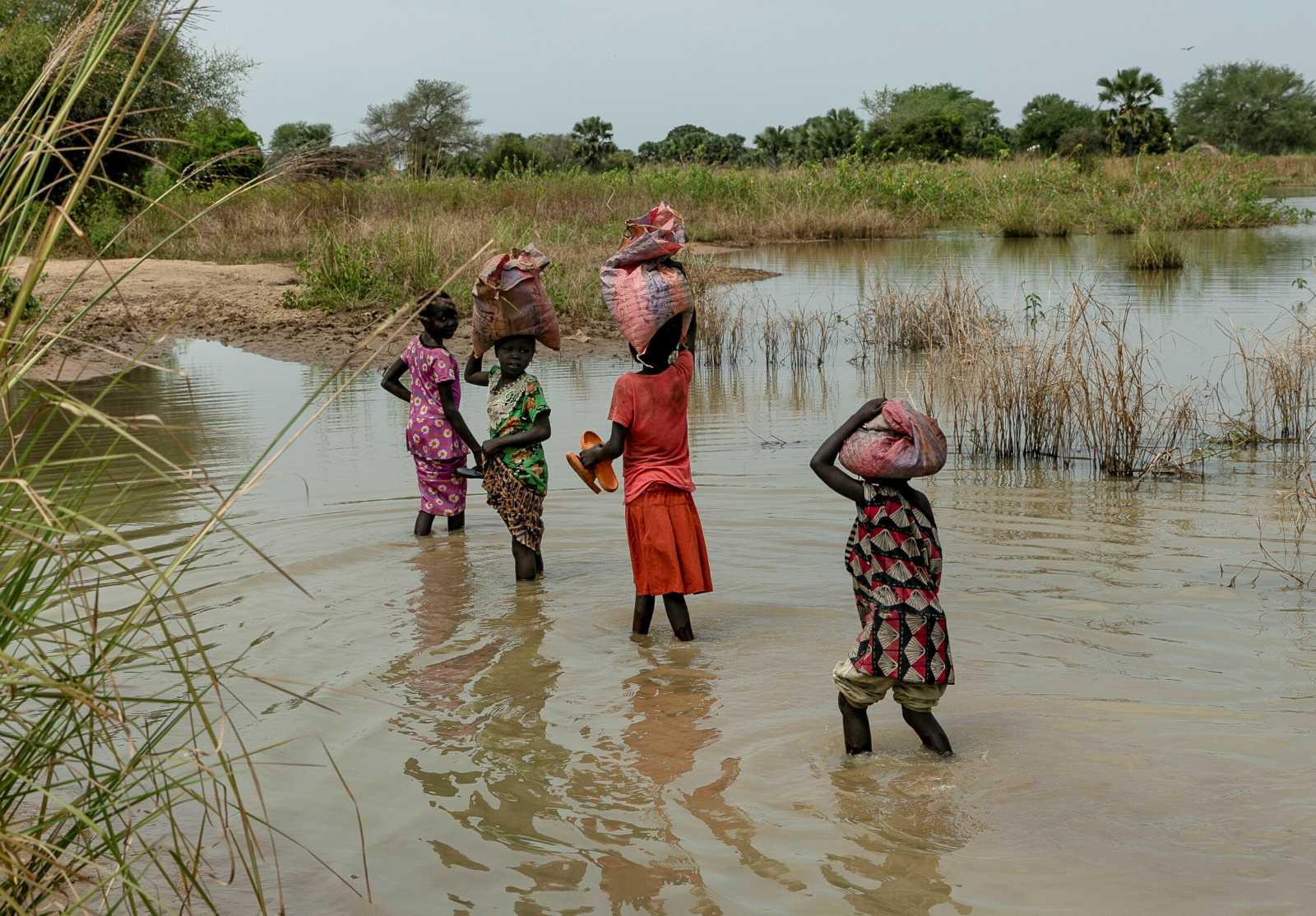 Kinder tragen 2021 ihre Habseligkeiten über ein überflutetes Feld im Bundesstaat Northern Bahr el Ghazal – das dritte Jahr in Folge, in dem die Region von schweren Überschwemmungen heimgesucht wurde.