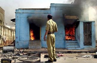 Polizist beobachtet, wie muslimische Geschäfte während der Krawalle von 2002 in Ahmedabad brennen.  