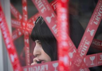 An Iranian woman with a mobile phone outside a café in Tehran in April 2026. The windows are covered with tape to prevent them from shattering in the event of an explosion.