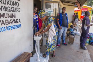 Eine Frau in Kigali, Ruanda, wäscht sich die Hände, ehe sie eine Busticket-Verkaufsstelle betritt.